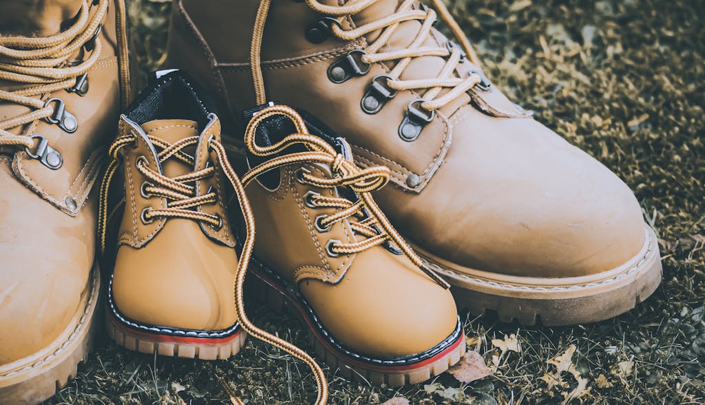 A close-up of father and child hiking boots on grassy ground, symbolizing family adventure.