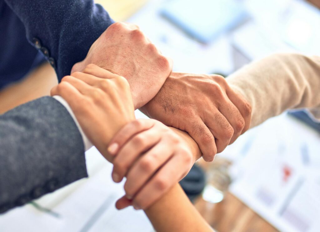 Close-up of diverse hands joining together over a table in an office setting, symbolizing teamwork and cooperation.